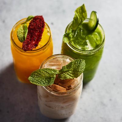 Three vibrant drinks in jars on a gray surface.
