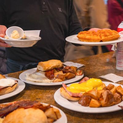 A server holding a plate of waffles over a counter filled with breakfast dishes.