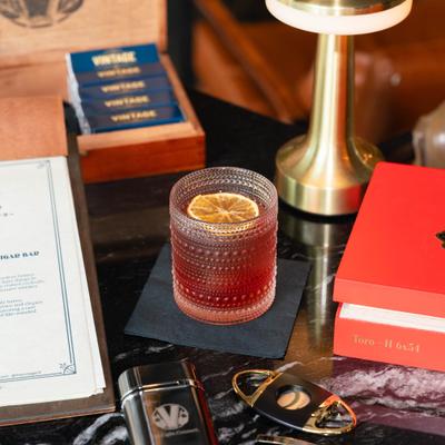 Cocktail with citrus in a textured glass on a marble table with red box, lighter and cigar cutter