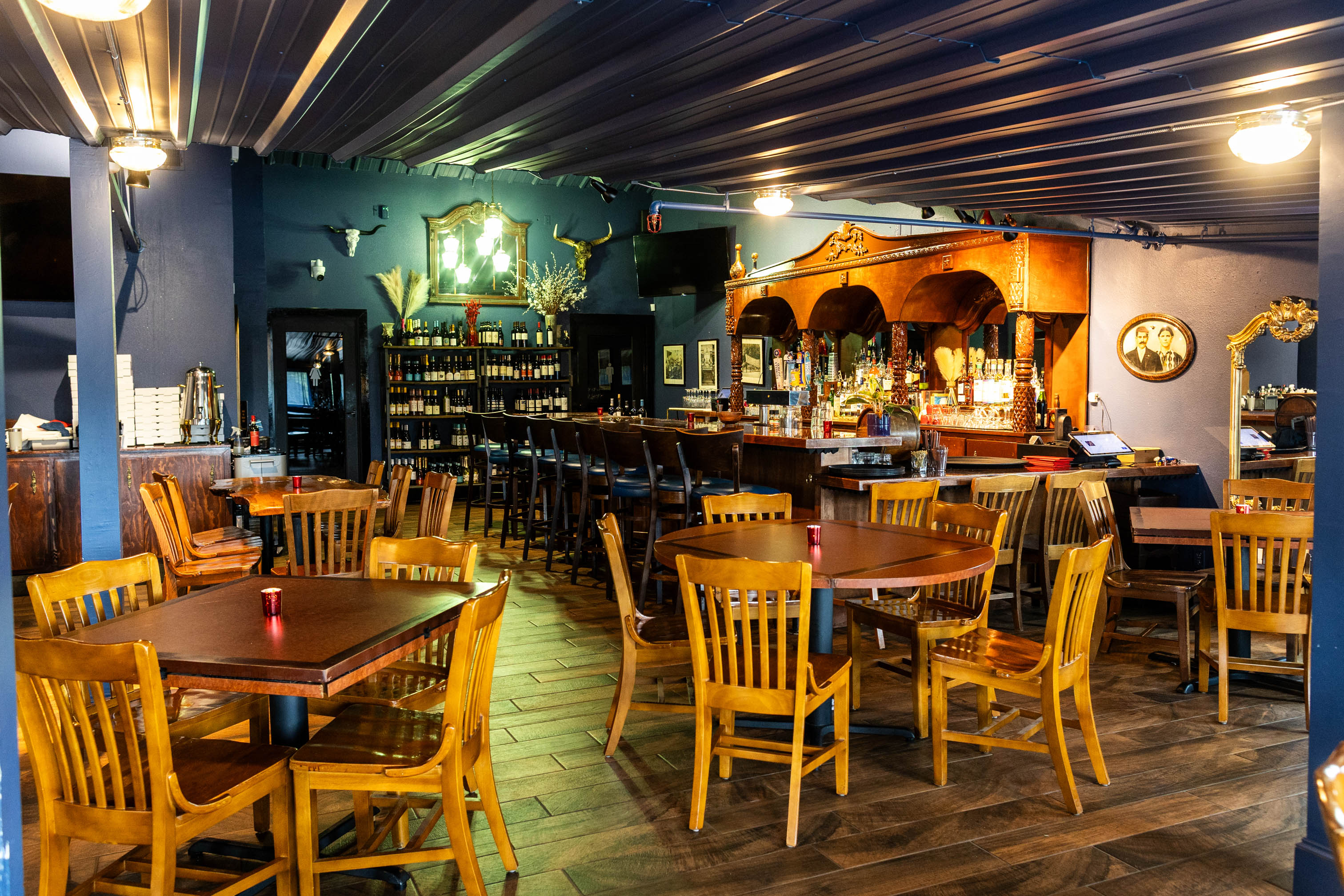 Warmly lit restaurant interior with wooden tables and chairs, bar and bar chairs