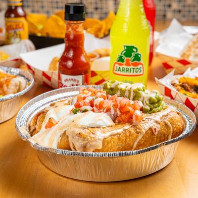 Chimichanga served in a foil dish, alongside bottles of Mexican soda and hot sauce.