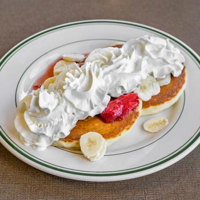Mini stack pancakes (2) covered with strawberries, bananas and whip cream.