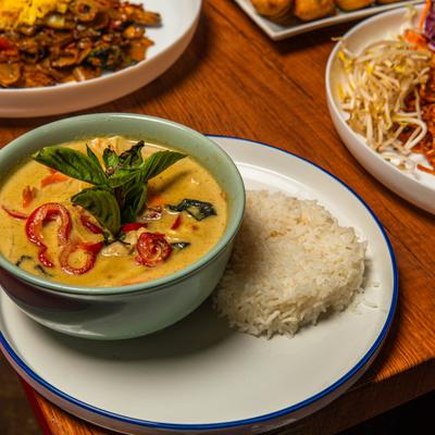 Green Curry garnished with fresh basil and served with a side of rice.