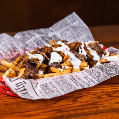Basket of loaded fries topped with steak and a white sauce.