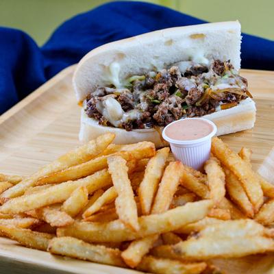 Philly cheesesteak sub with fries and a cup of sauce.