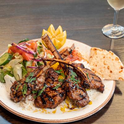 Grilled lamb chops served with salad, rice, and flatbread.