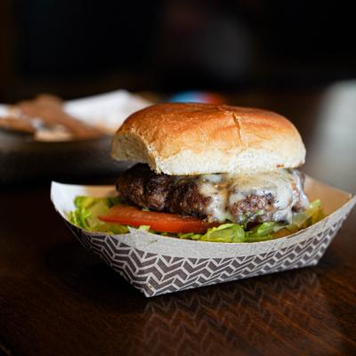 Cheeseburger served on a soft bun with lettuce and tomato in a paper food tray.