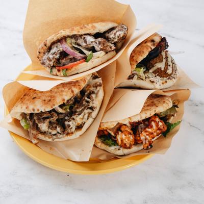 Selection of pita sandwiches filled with meat and various fresh vegetable toppings.