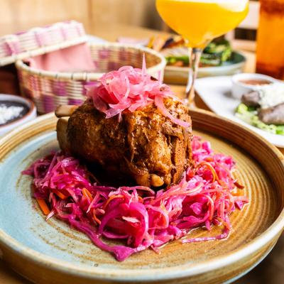 Braised pork shank with spicy red slaw and pickled onions on top.