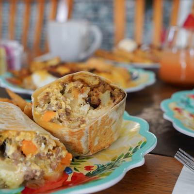 A halved burrito with other breakfast dished in the background.