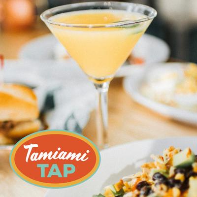 Pale cocktail in a martini glass beside plated food.