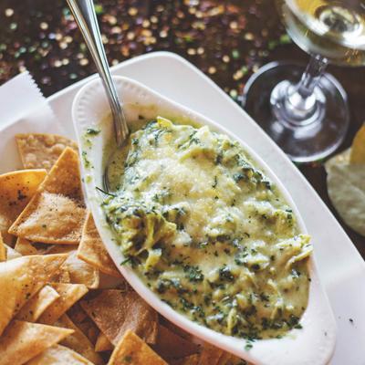 Creamy green dip with tortilla chips on the side, accompanied by a glass of white wine