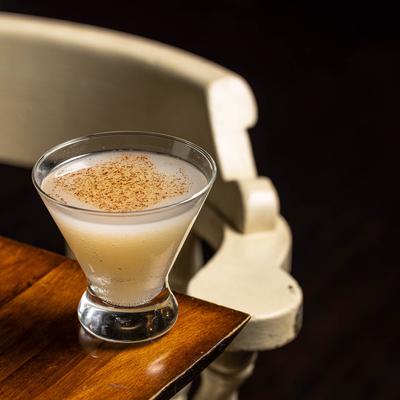 A glass of Lira cocktail sitting on table corner inside.