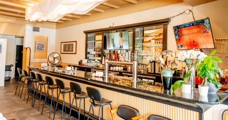 Interior view of a bar area with a sleek black counter, bar stools, mounted TVs
