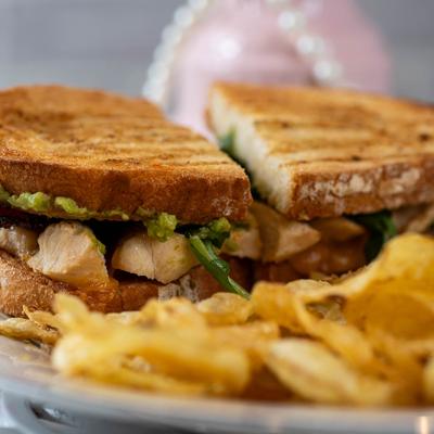 Grilled chicken bacon avocado sandwich served with chips.