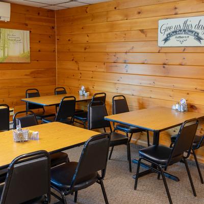 Dining area with multiple wooden tables and chairs, wood-paneled walls, and inspirational wall art.