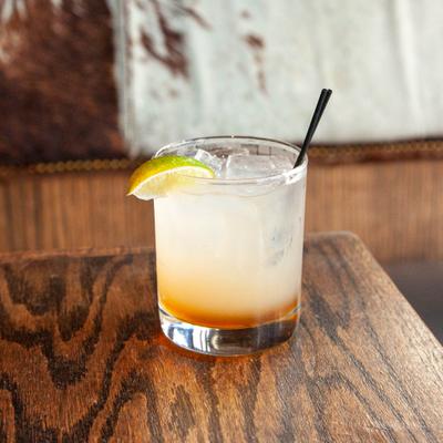 Pale cocktail served with lime on wooden table