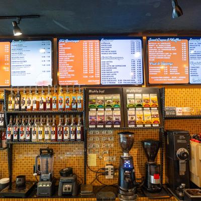 View at the bar with coffe machine, shelves with bottles and menu boards.
