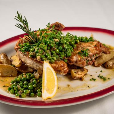 Roasted chicken on a plate with peas, potatoes, lemon, and rosemary.