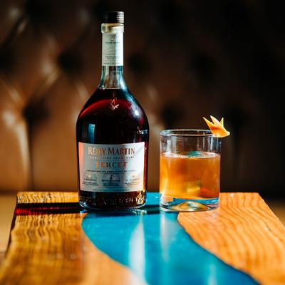 A bottle of cognac beside a full glass on a wooden table with blue details.