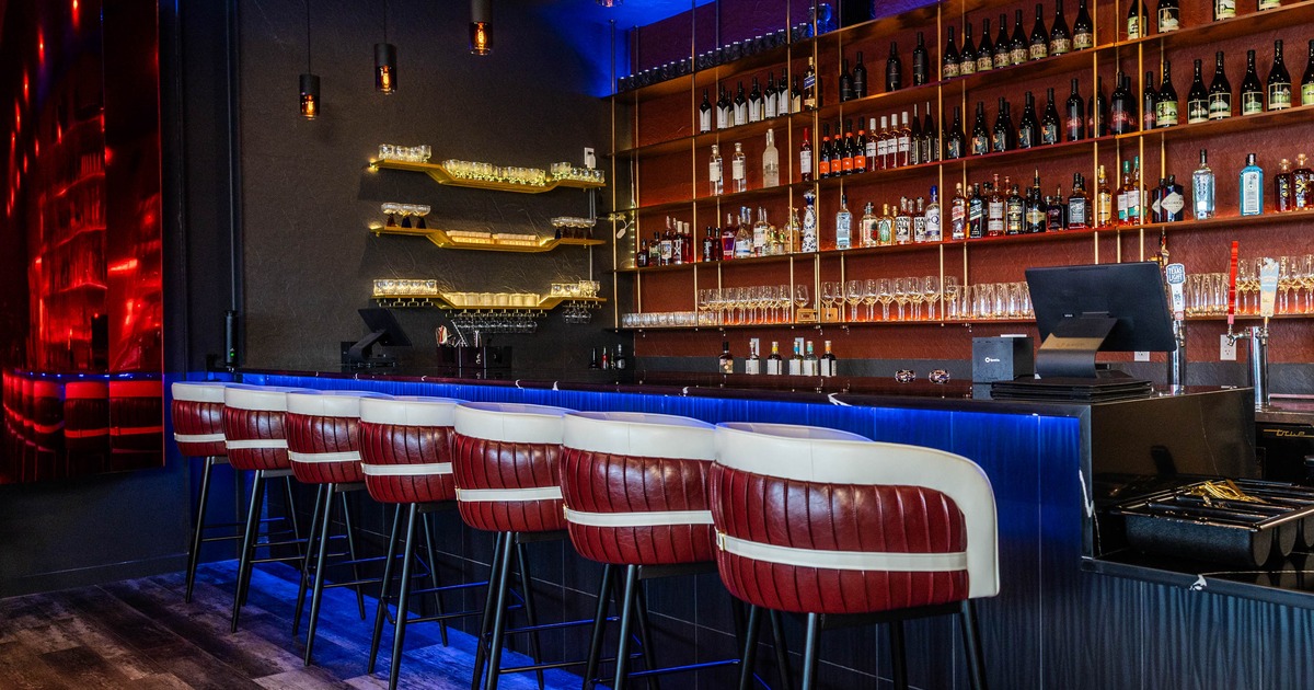Modern interior - red and white bar stools, a blue-lit counter and shelves stocked with bottles