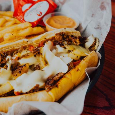 Philly cheesesteak sandwich served with fries and dipping sauce.