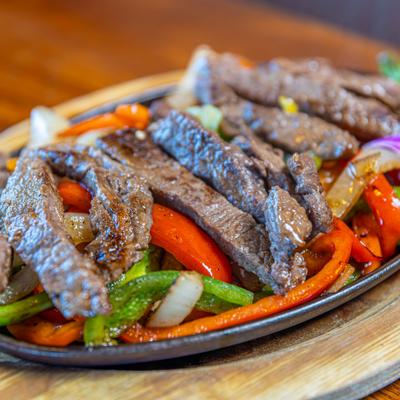 Steak fajitas with vegetables on a sizzling platter.