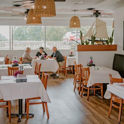 Bright dining room featuring white tablecloths, large windows, and seated guests.