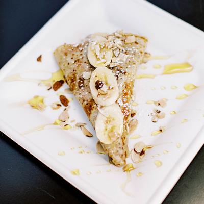 Crepe topped with crushed almonds, banana slices, honey, and powdered sugar.