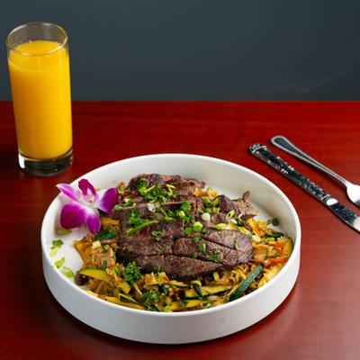 Veggie Bowl topped with grilled steak and served alongside a glass of orange juice.