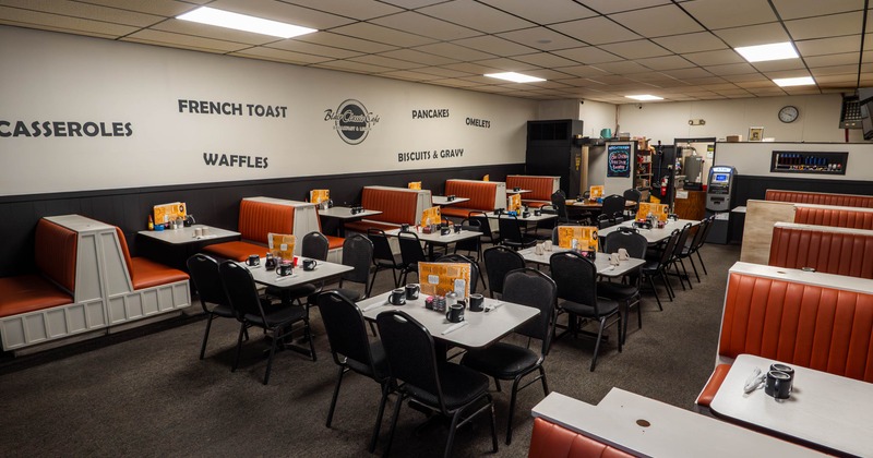 A retro-style diner interior with red booths, black chairs and white tables.