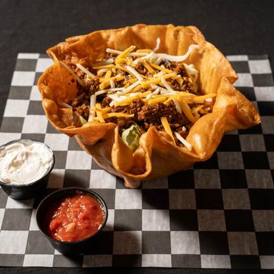 Taco salad served with red salsa and sour cream on a checkered paper.