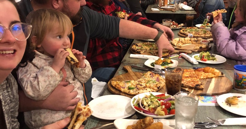 People gathered around a table with assorted pizzas