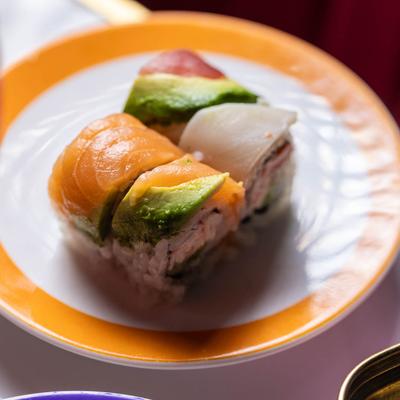 Close-up of sushi rolls topped with salmon, avocado, and fish on a white plate with an orange rim.
