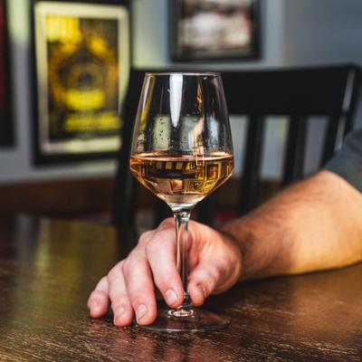 A person holding a glass of white wine at table.