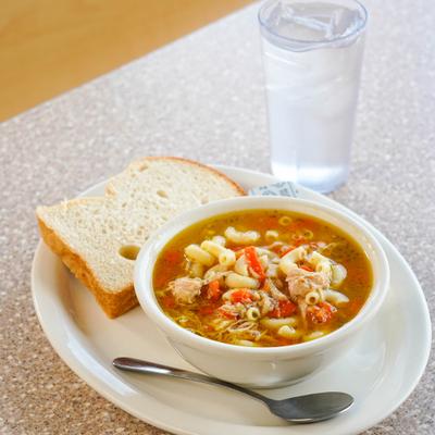 Chicken noodle soup served with a slice of bread and a drink.