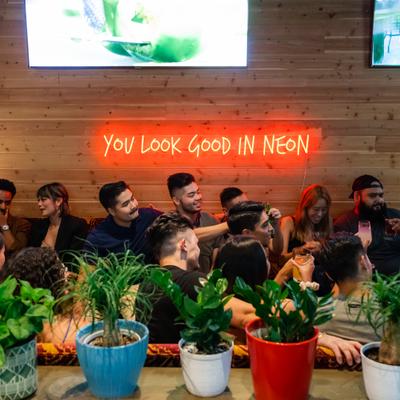 Group of guests in the seating area with plant pots in front and TVs and neon light wall sign
