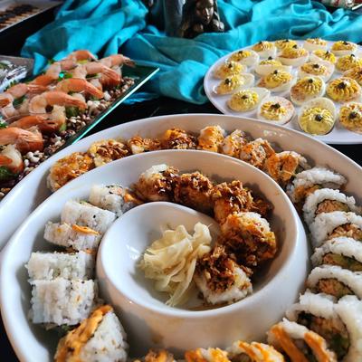 Assorted sushi rolls, shrimp, and deviled eggs on platters.