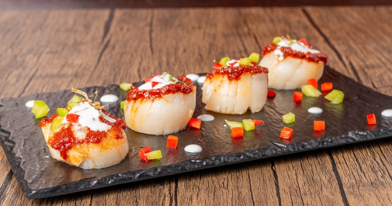 Pan-seared scallops topped with a sauce, diced peppers and fresh herbs