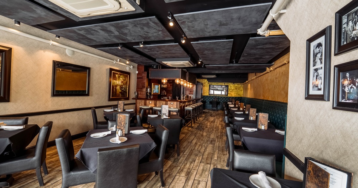 A modern interior - black tables and chairs, wooden flooring and a bar area with pendant lights