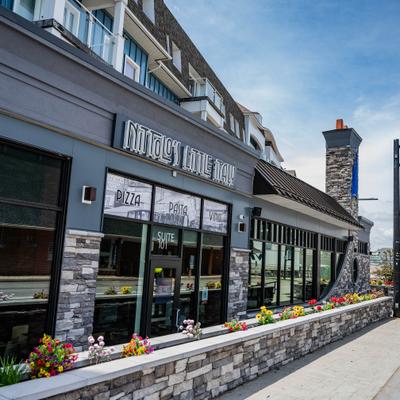 Storefront featuring gray stone siding with flowers, entrance and signage.