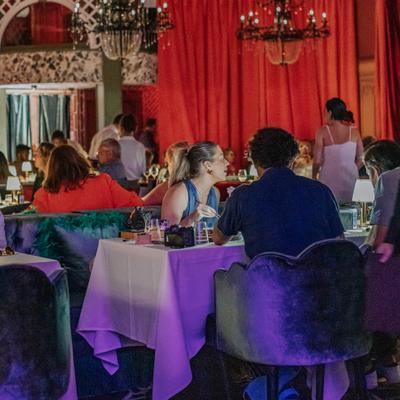 Full restaurant with guests dining red curtains and chandeliers in view.
