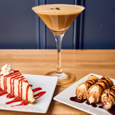 Cheesecake slice topped with strawberry sauce, alongside cannoli and Espresso Martini.