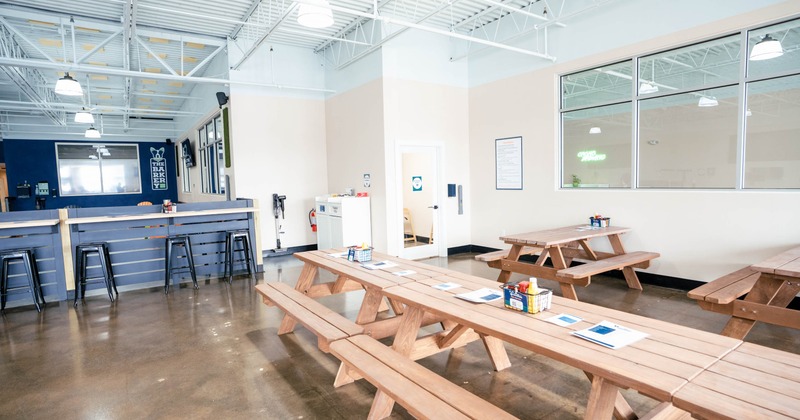 An indoor area with picnic tables, a blue counter, high ceilings, and polished concrete floor