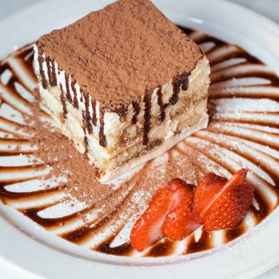 Tiramisu dusted with cocoa powder, drizzled with chocolate sauce, and garnished with strawberries.