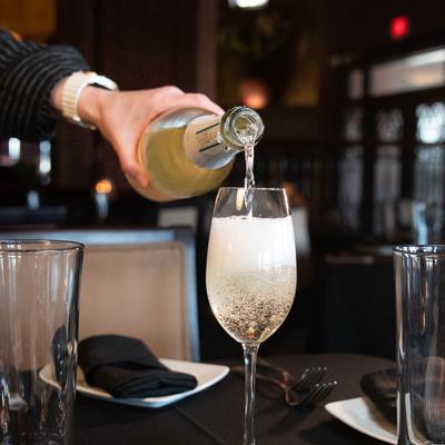 A server pours sparkling wine into a flute on a dimly lit restaurant table.