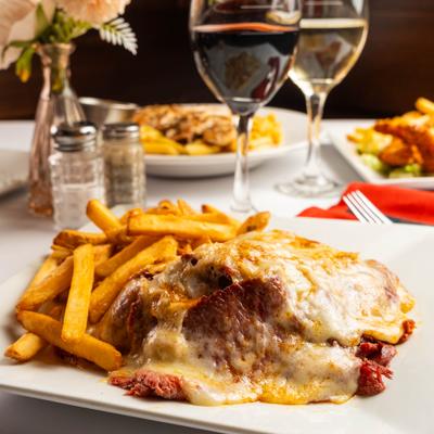 Pastrami sandwich covered in cheese served with fries and wine