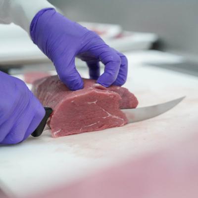 Person slicing raw beef on a cutting board, close view.