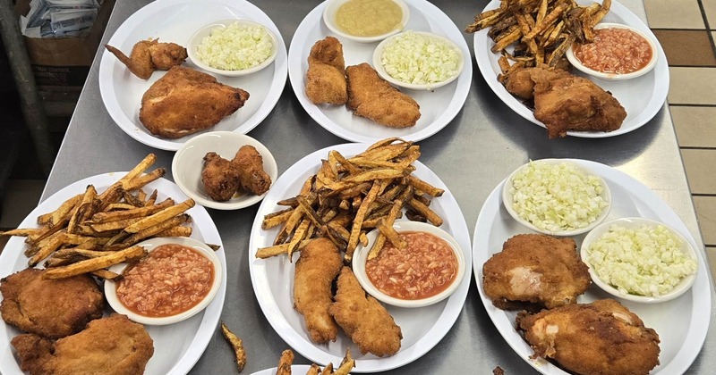 Several fried chicken dinner plates arranged with fries, coleslaw, and tomato rice