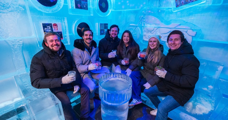Interior of an ice lounge with blue lighting, ice walls, benches with throws, and artistic carvings